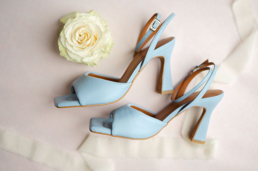 A flat lay detail photo of light blue heels for a bride's "something blue" on top of a pink mat with a white rose and white ribbon.