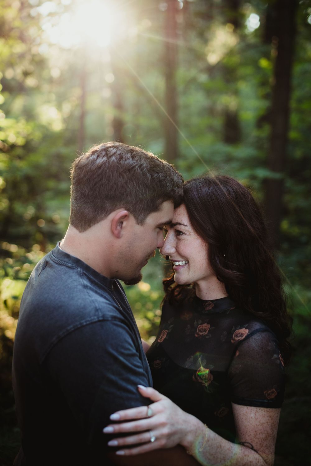 A romantic couple shares an intimate moment in sunlit forest.