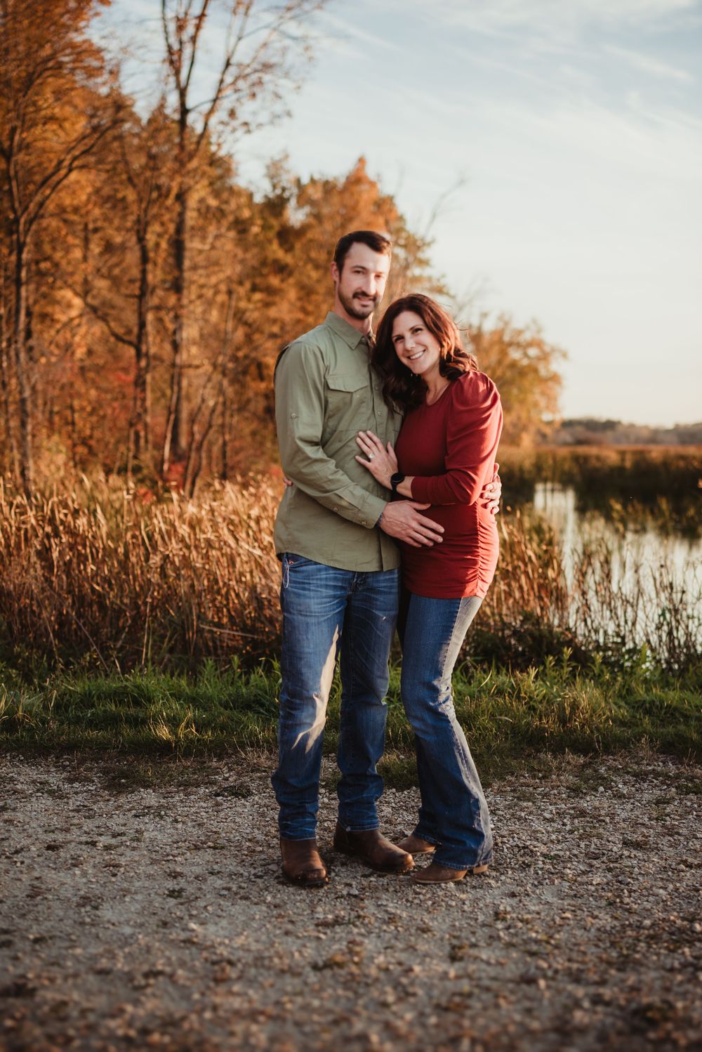 A couple embraces in front of fall foliage and a lake during sunset.