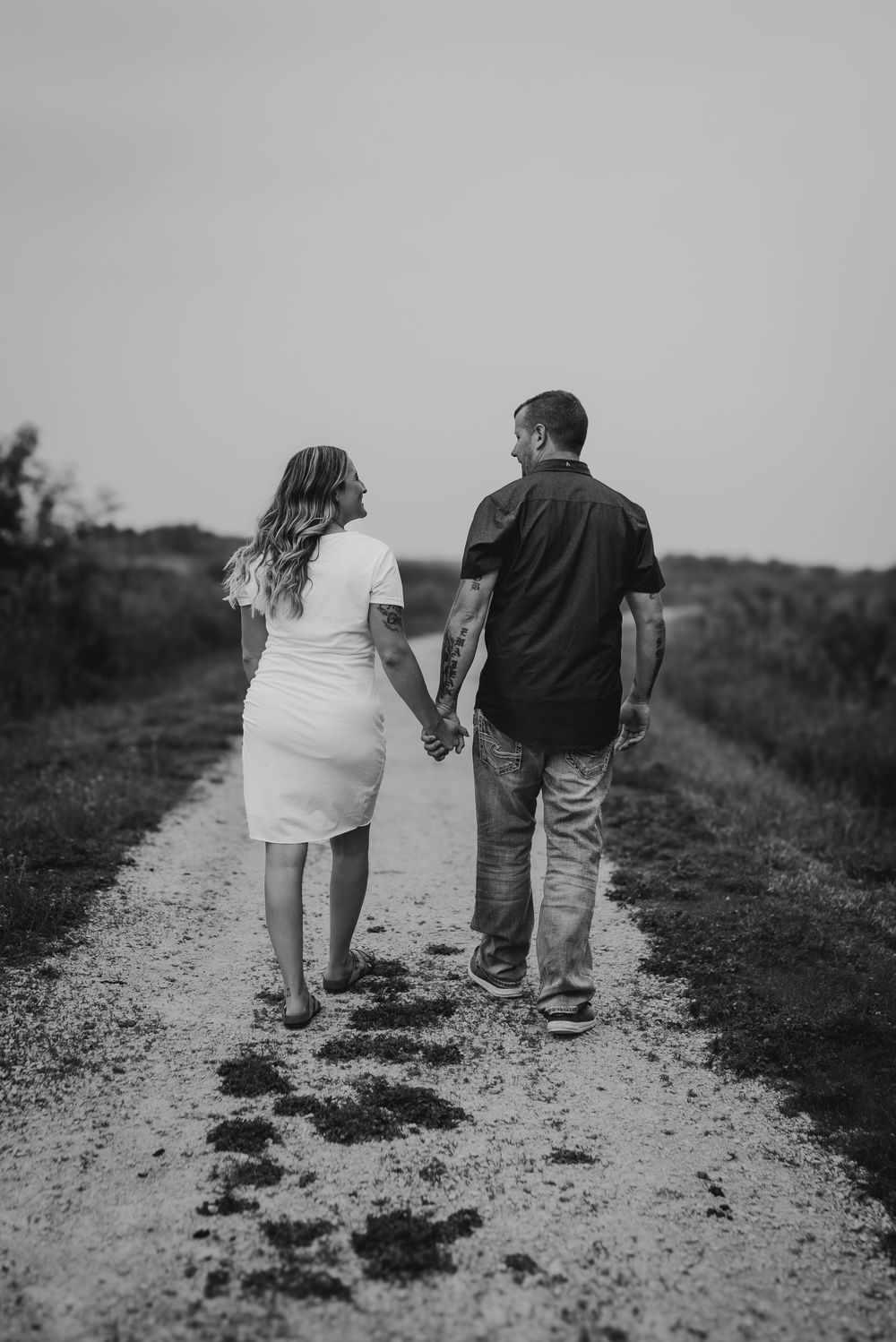 A couple walks hand in hand down a gravel path in black and white photography.