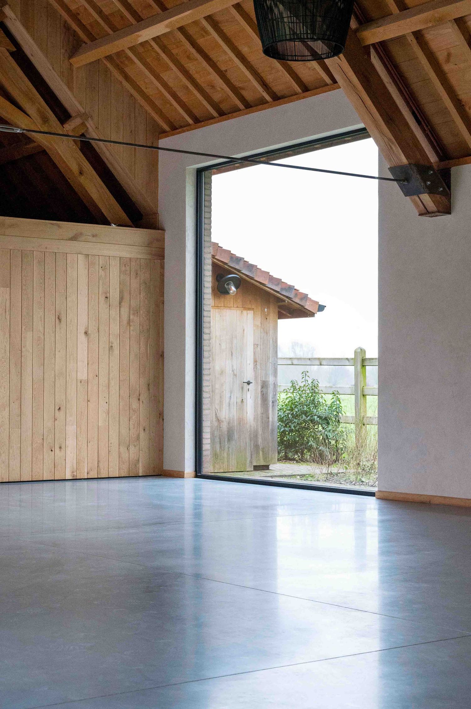 Spacious room with wooden ceiling beams and floor-to-ceiling windows overlooking outdoor scenery.