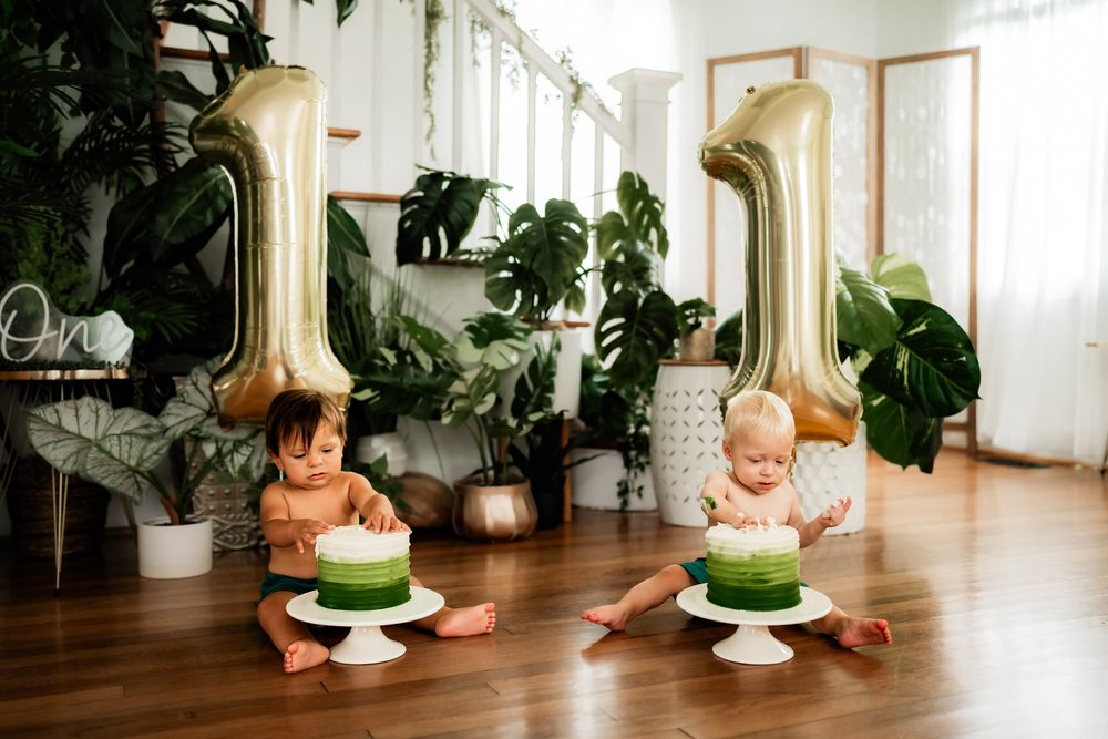 Birthday cake with green and white frosting displayed on a white cake stand surrounded by indoor plants.