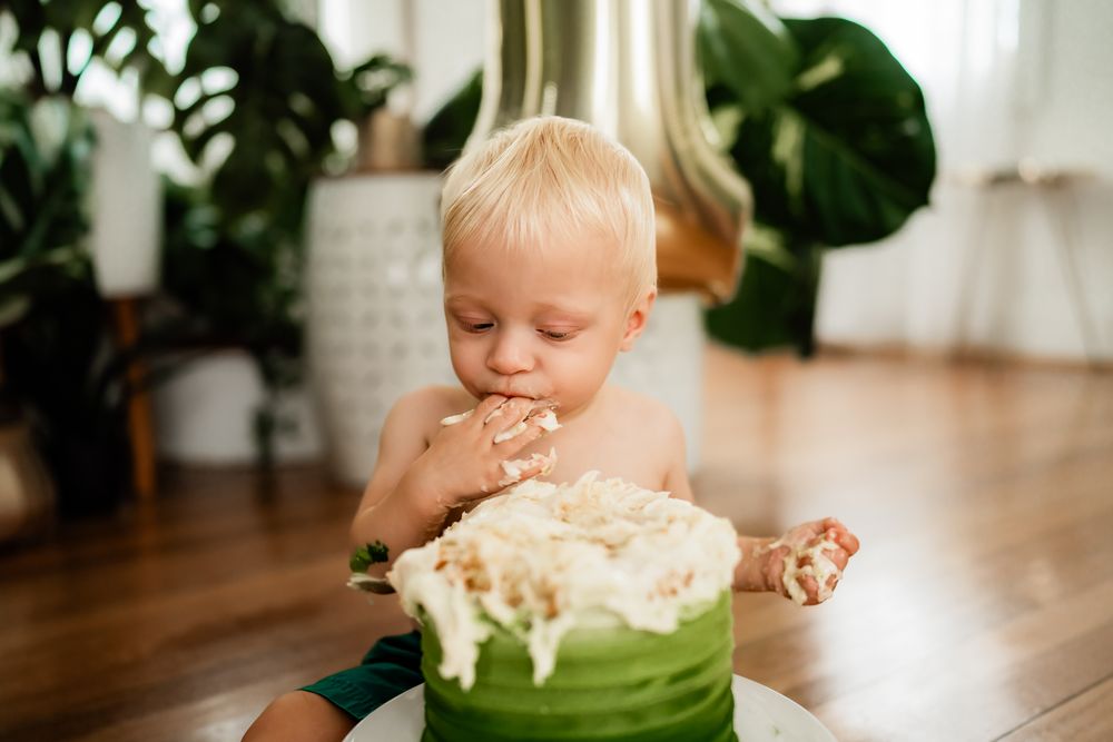 Baby smashing and playing with cake at a first birthday cake smash photo session in bright indoor setting.