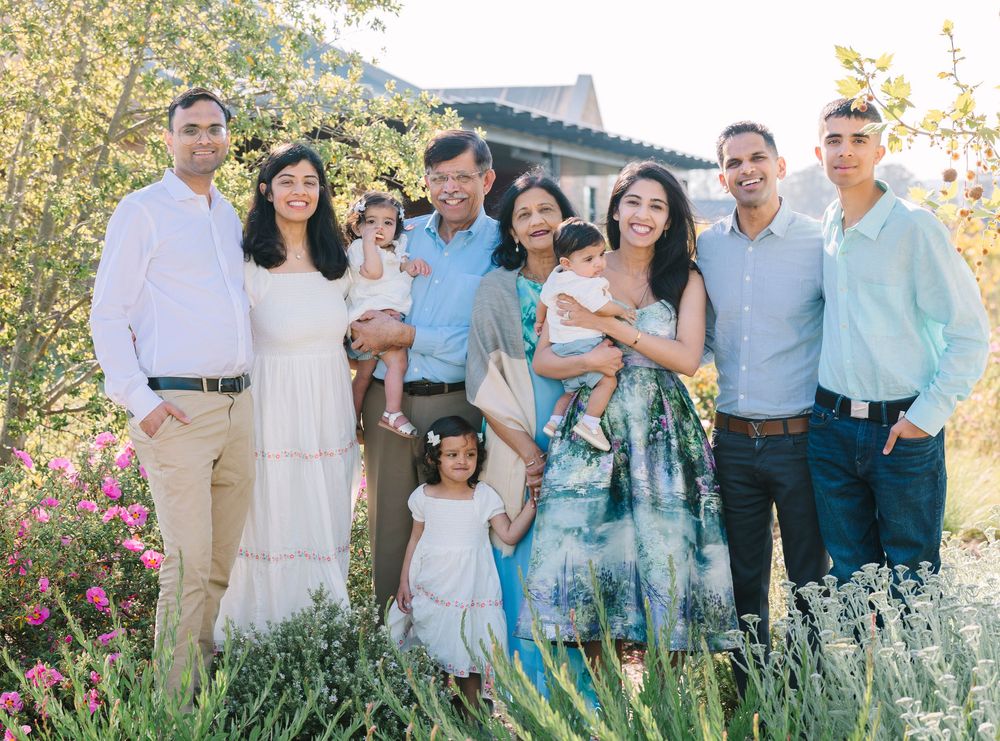 Extended family gathering outdoors in a garden with blooming flowers and greenery.