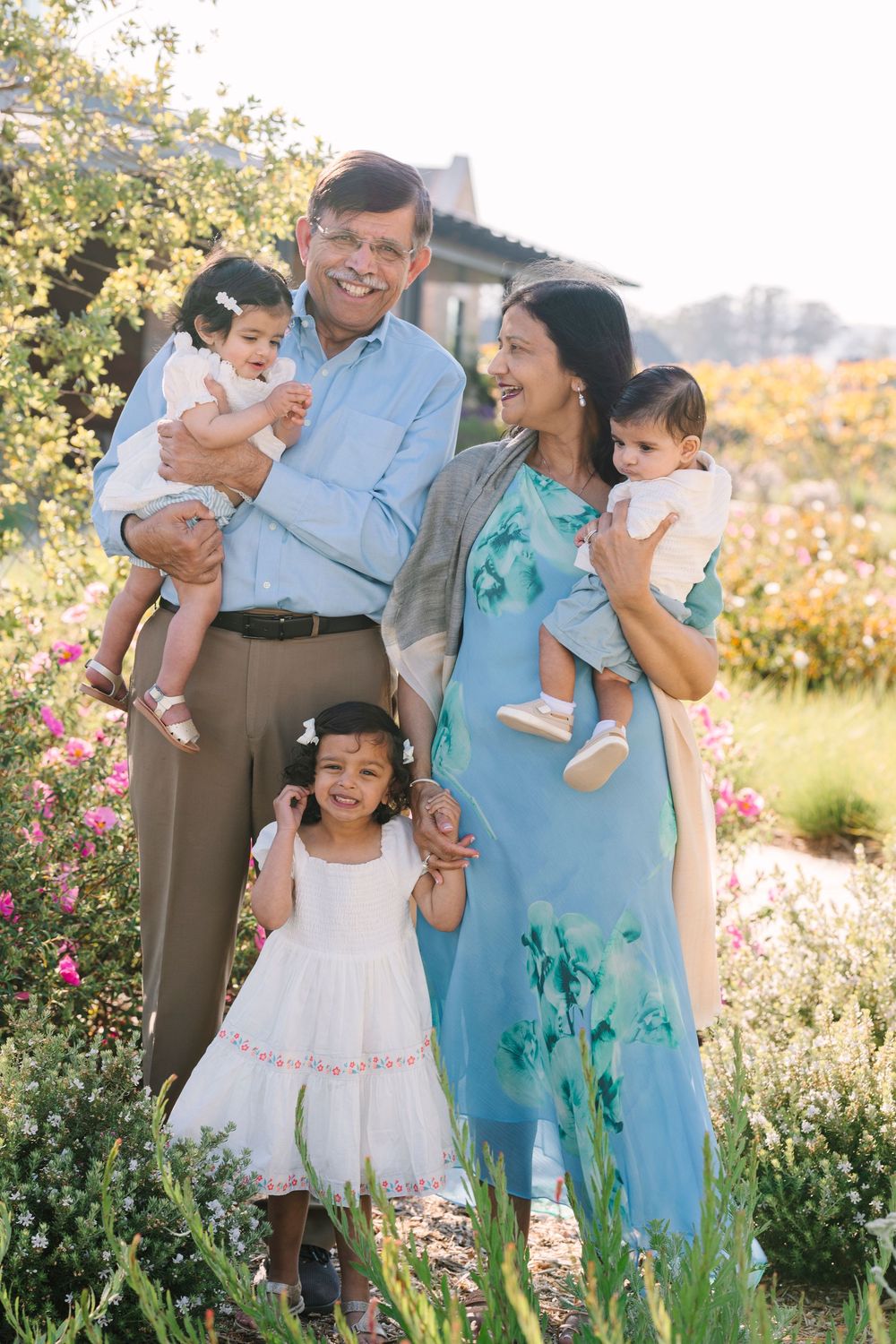Family portrait session in blooming garden with pink flowers and natural sunlight.