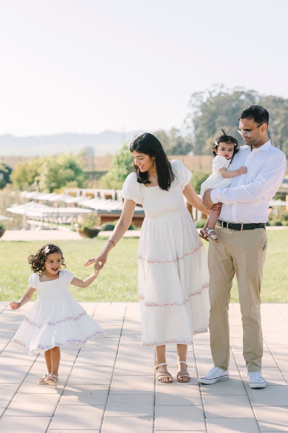 Sweet family dancing together on a paved outdoor area in matching white outfits.