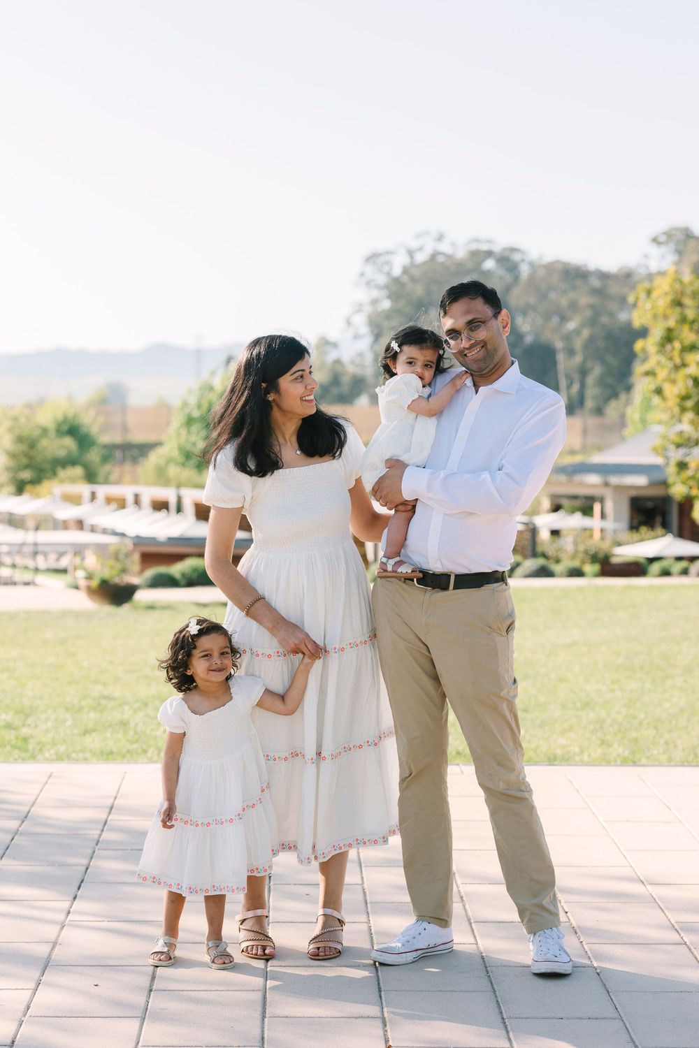 Candid moments of a family dancing and playing together outdoors in white attire.