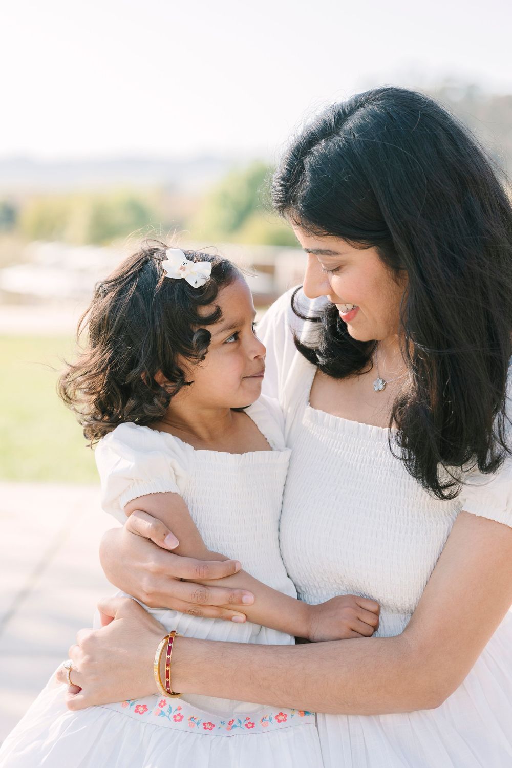 Tender embraces between parent and child in white outfits against a sunny outdoor backdrop.
