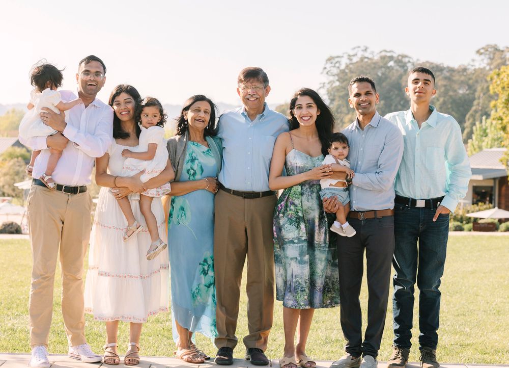 Extended family group photo outdoors with coordinated outfits in white, blue and tan colors.