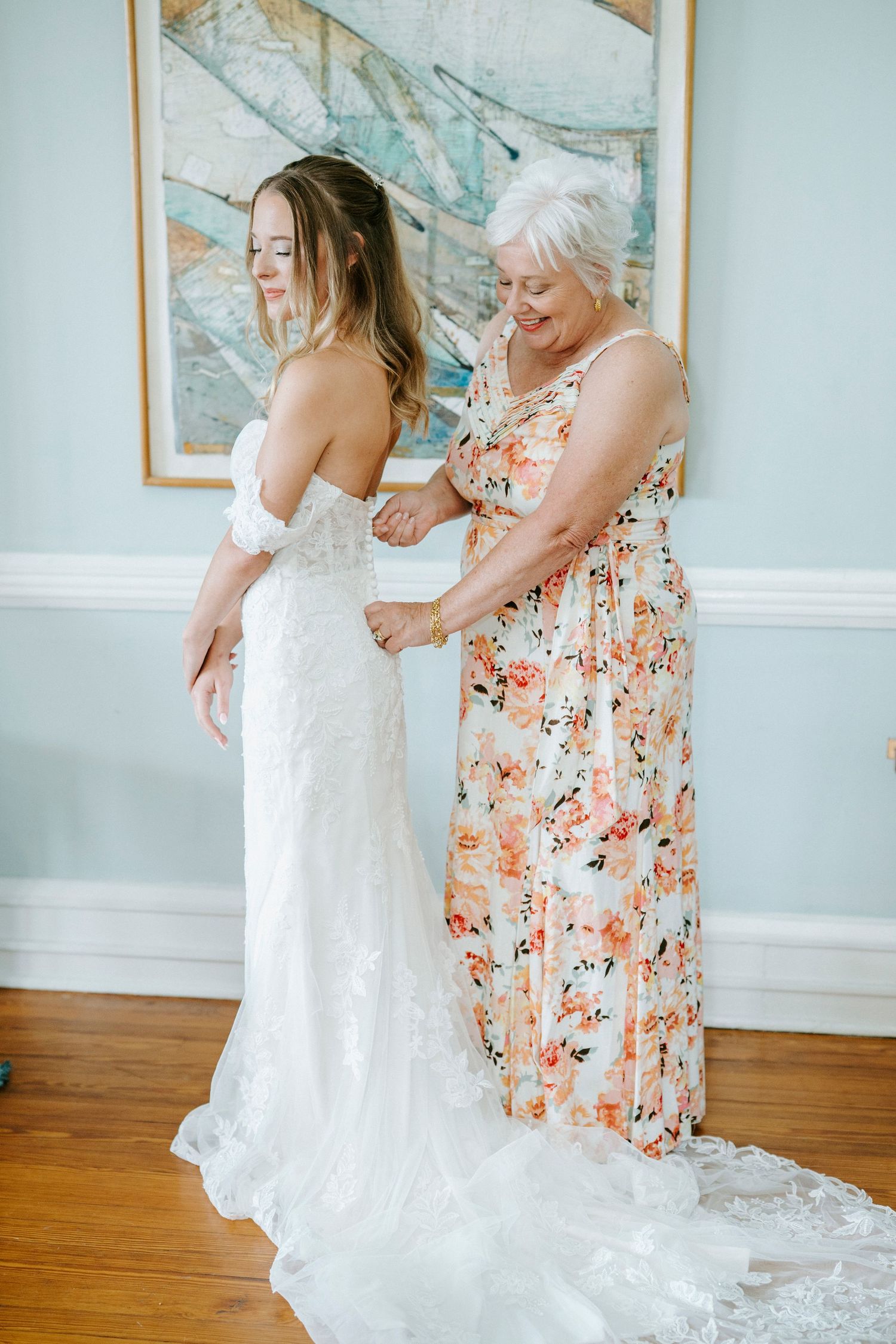 A sequence shows a touching moment as a white wedding dress is fitted and adjusted in an elegant room with artwork.