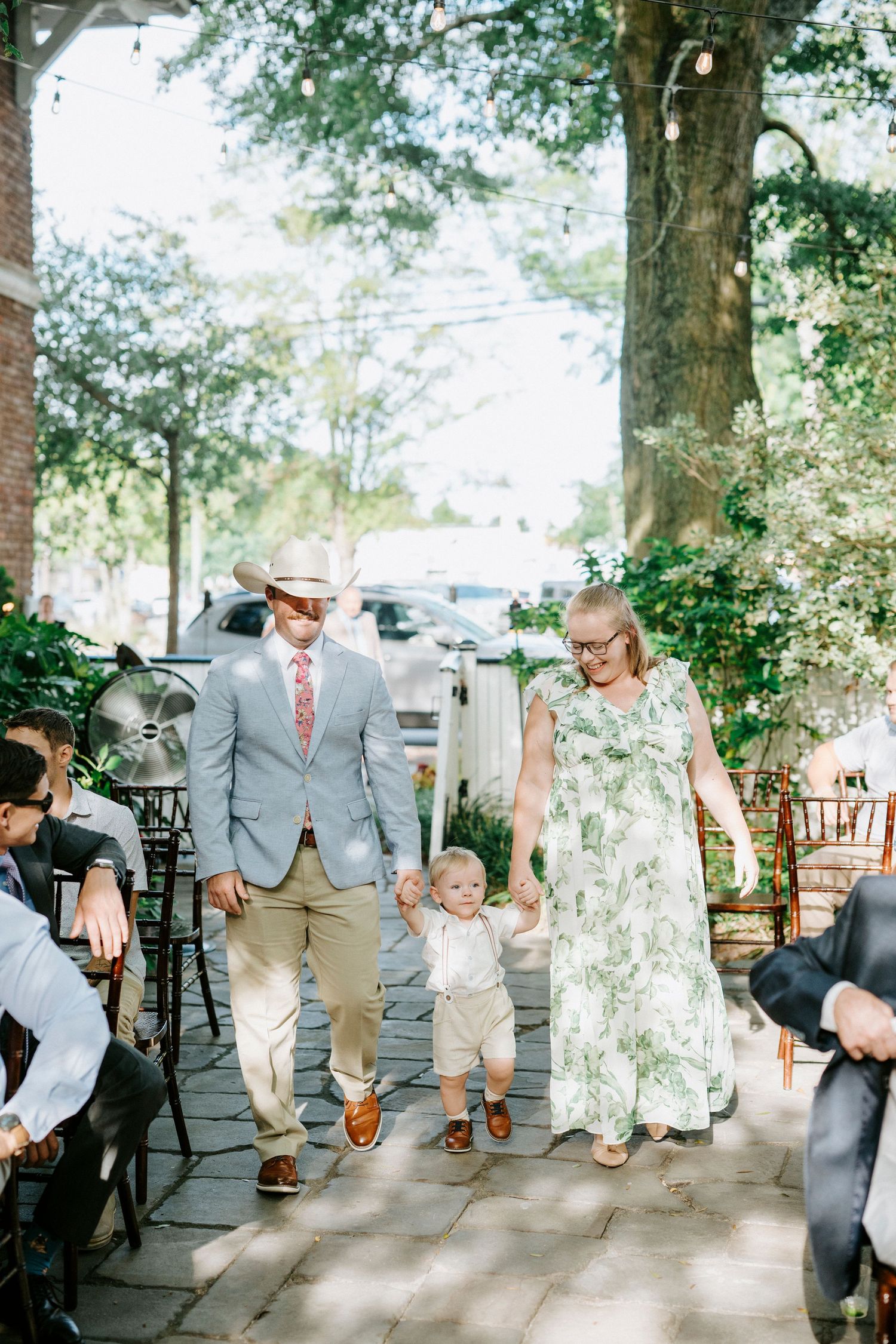 A playful sequence of wedding party members jumping in a line on a tree-lined pathway outdoors.