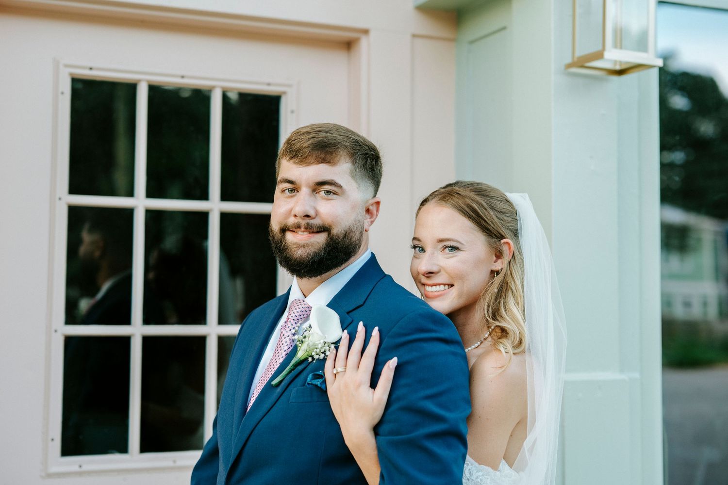 Wedding couple and guests share candid laughing moment outside in front of white building.