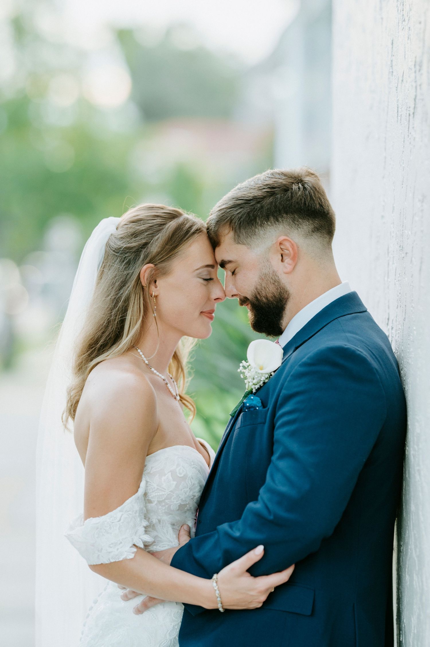 Intimate moment between newlyweds against a white pillar surrounded by greenery.