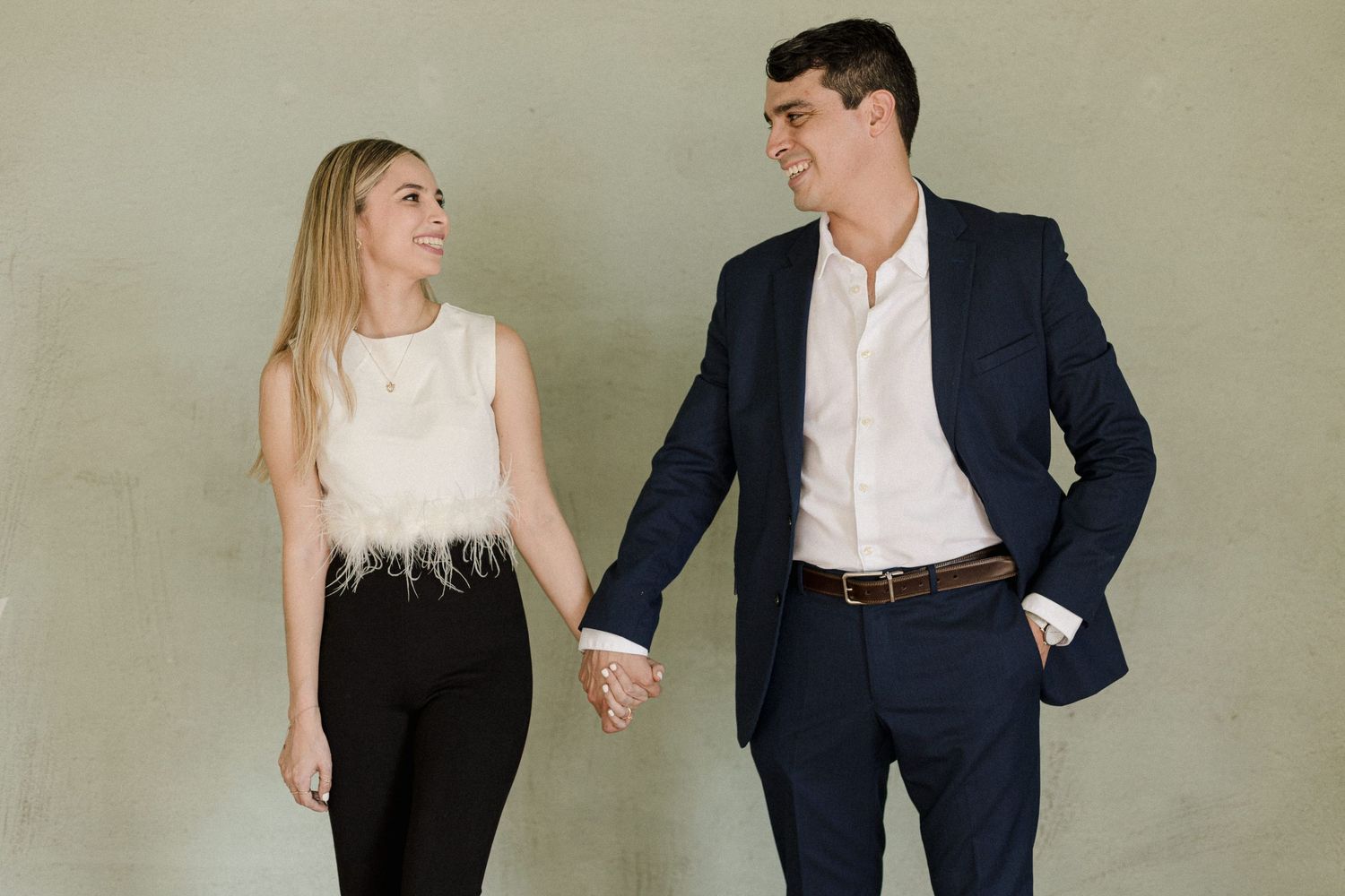 Professional couple in business attire poses playfully together against a neutral studio backdrop.
