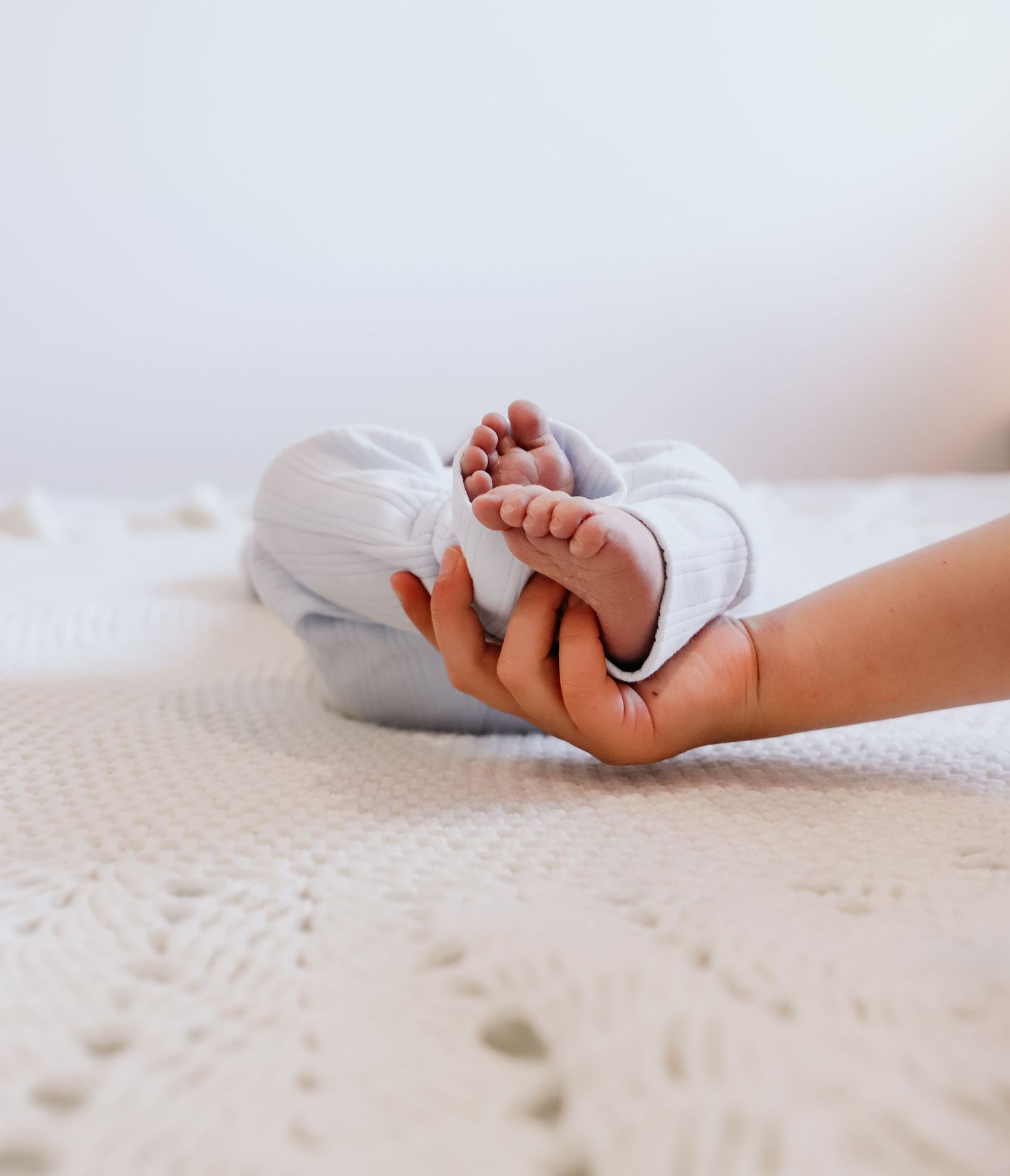 Tiny baby feet in white sock against soft white textured blanket background.