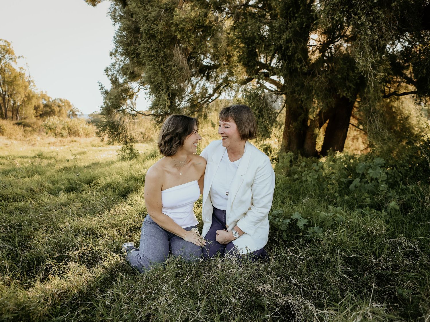 Mum and daughterintimately together in a sunlit meadow surrounded by trees and natural scenery.