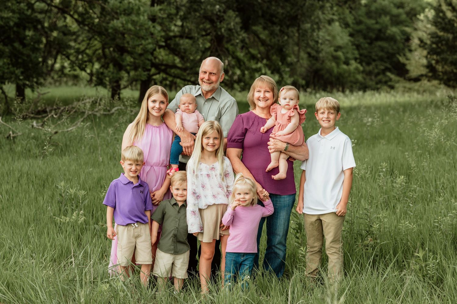Family members stand together on a grassy hill in casual attire for an outdoor photo session.