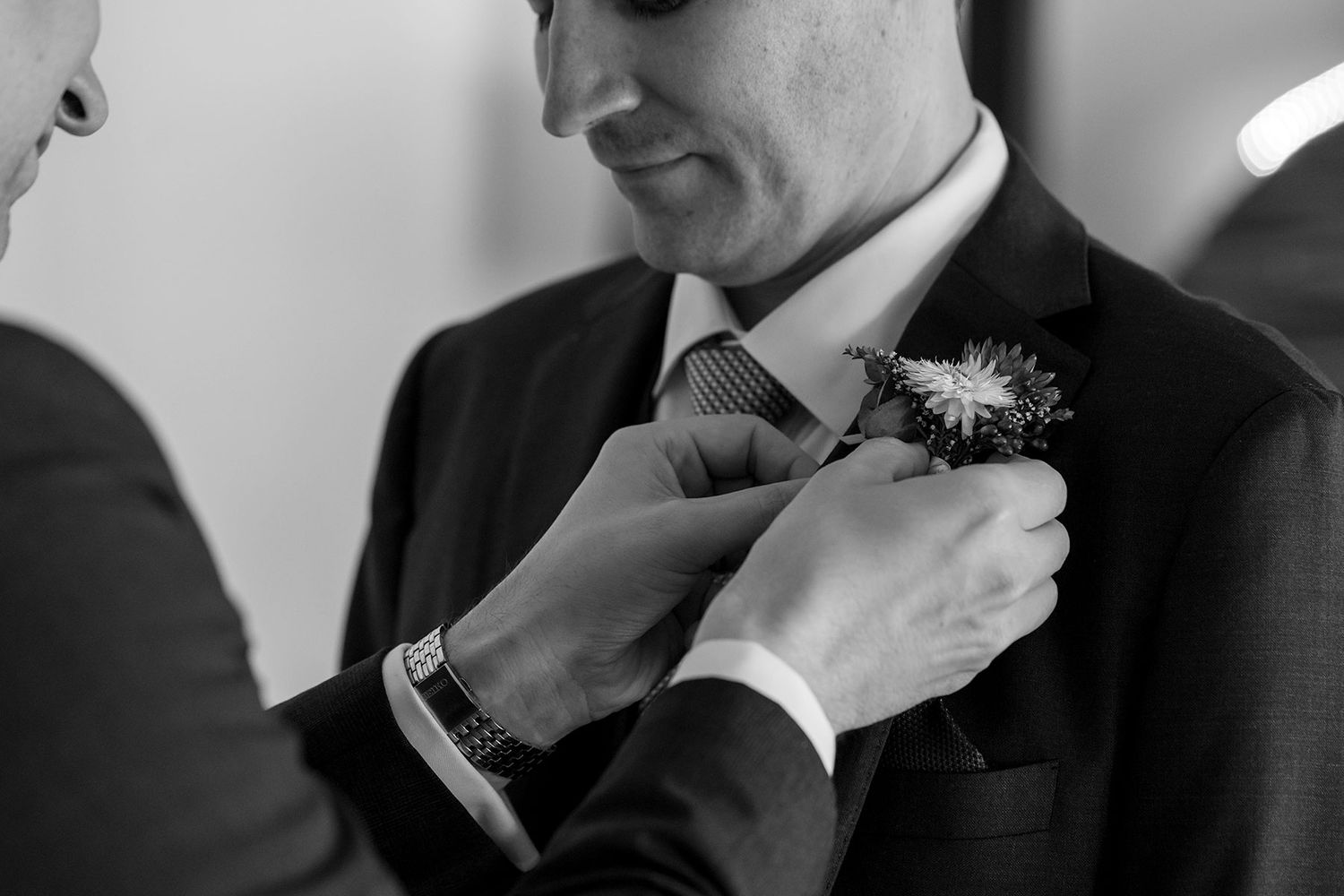 A close up image of a Groom with his groomsmen adjust their button hole flowers and collars in a black and white photo.