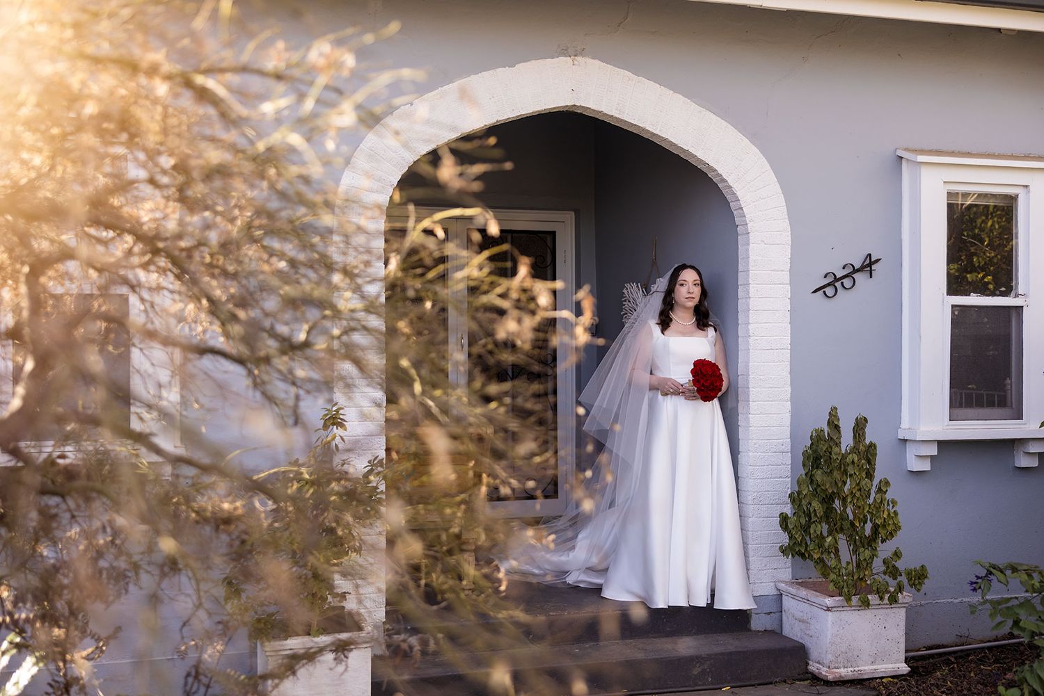A Bride wearing her Anna Campbell wedding dress stands in the old arch entrance of an Albury house soft sunlight in the tree leaves.
