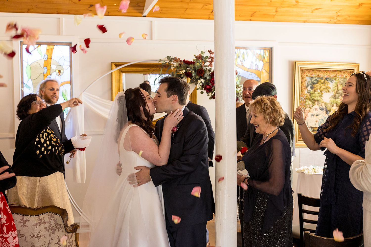 Wedding guests throw rose petals over the Bride and Groom as they share a kiss after their indoor wedding ceremony at La Maison Wodonga.