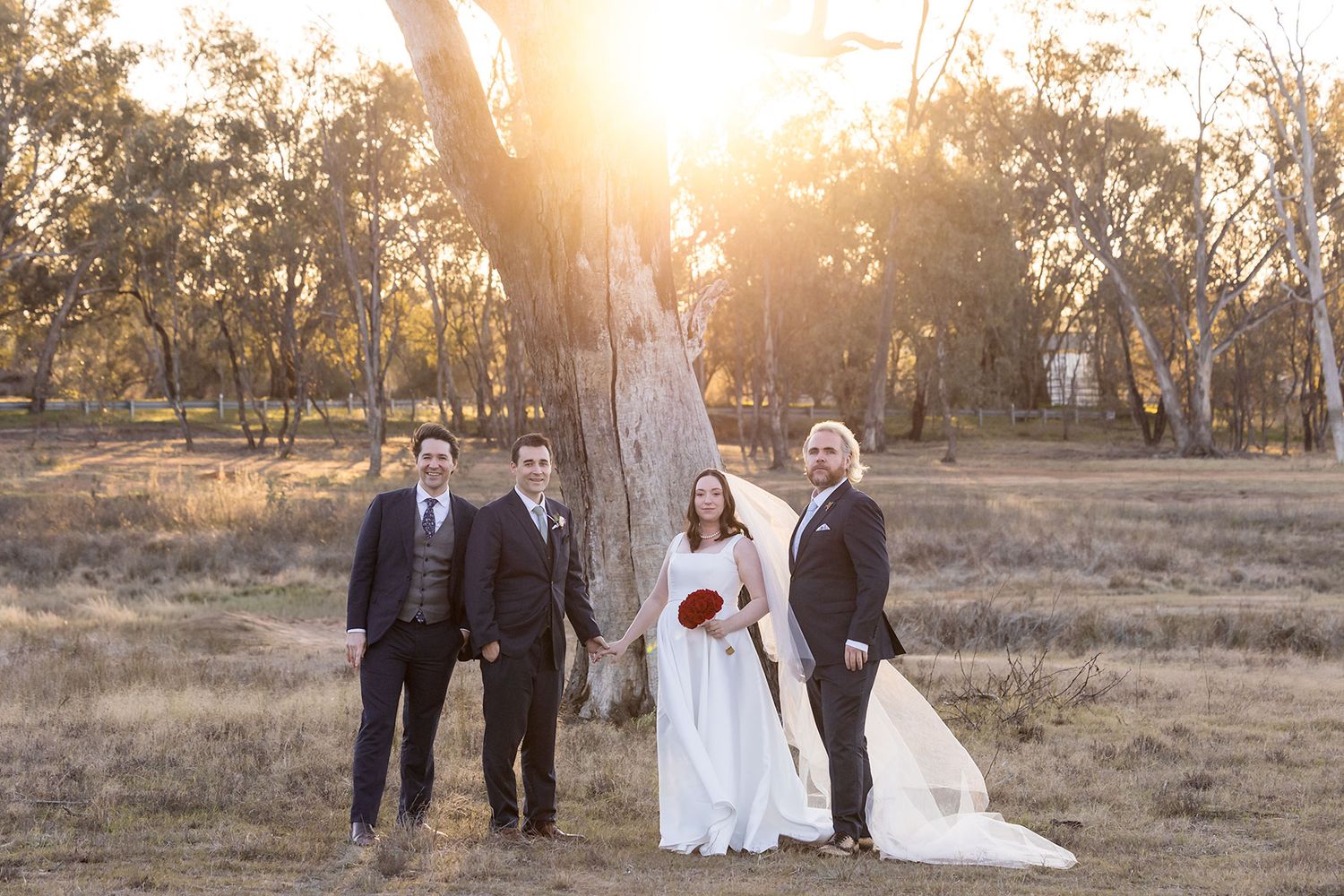 A wedding party walks through a sunlit field at golden hour, creating a romantic silhouetted scene.