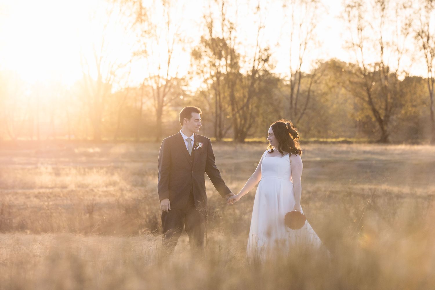 A glowing sunset silhouettes a couple holding hands in a outdoor setting during their romantic photoshoot.