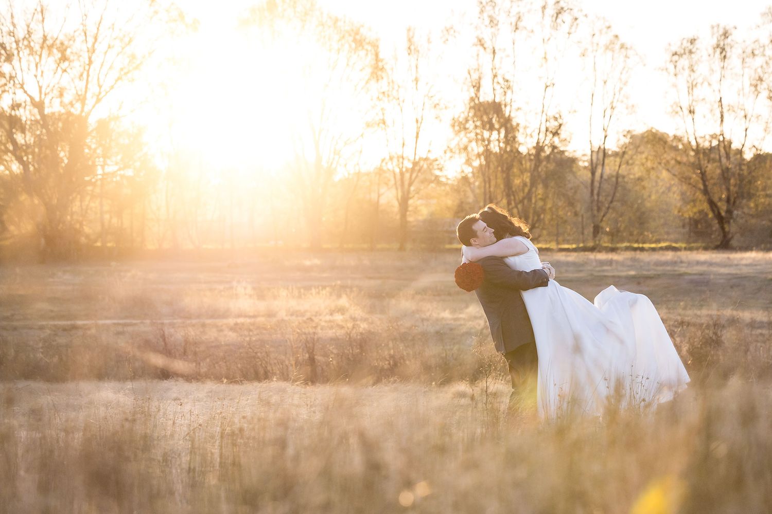 A romantic couple embraces in a golden sunlit field during sunset while soft light surrounds them creating a dreamy atmosphere.