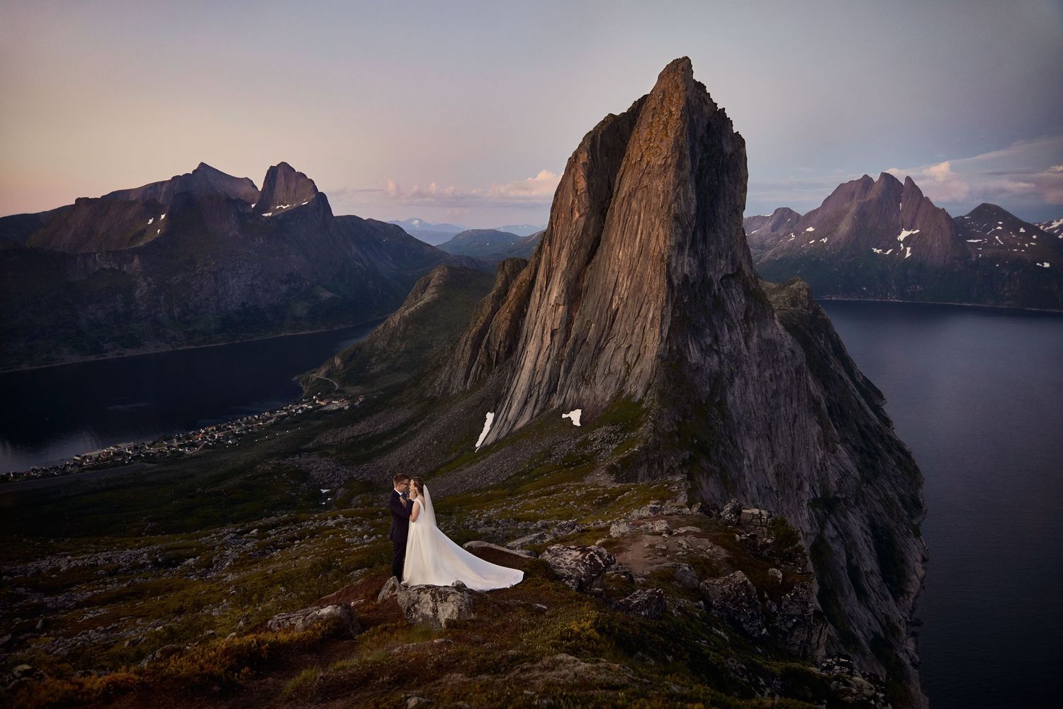 Bride and groom with mountain Segla, Senja in the background in pastel colored midnight sun in scenic surroundings