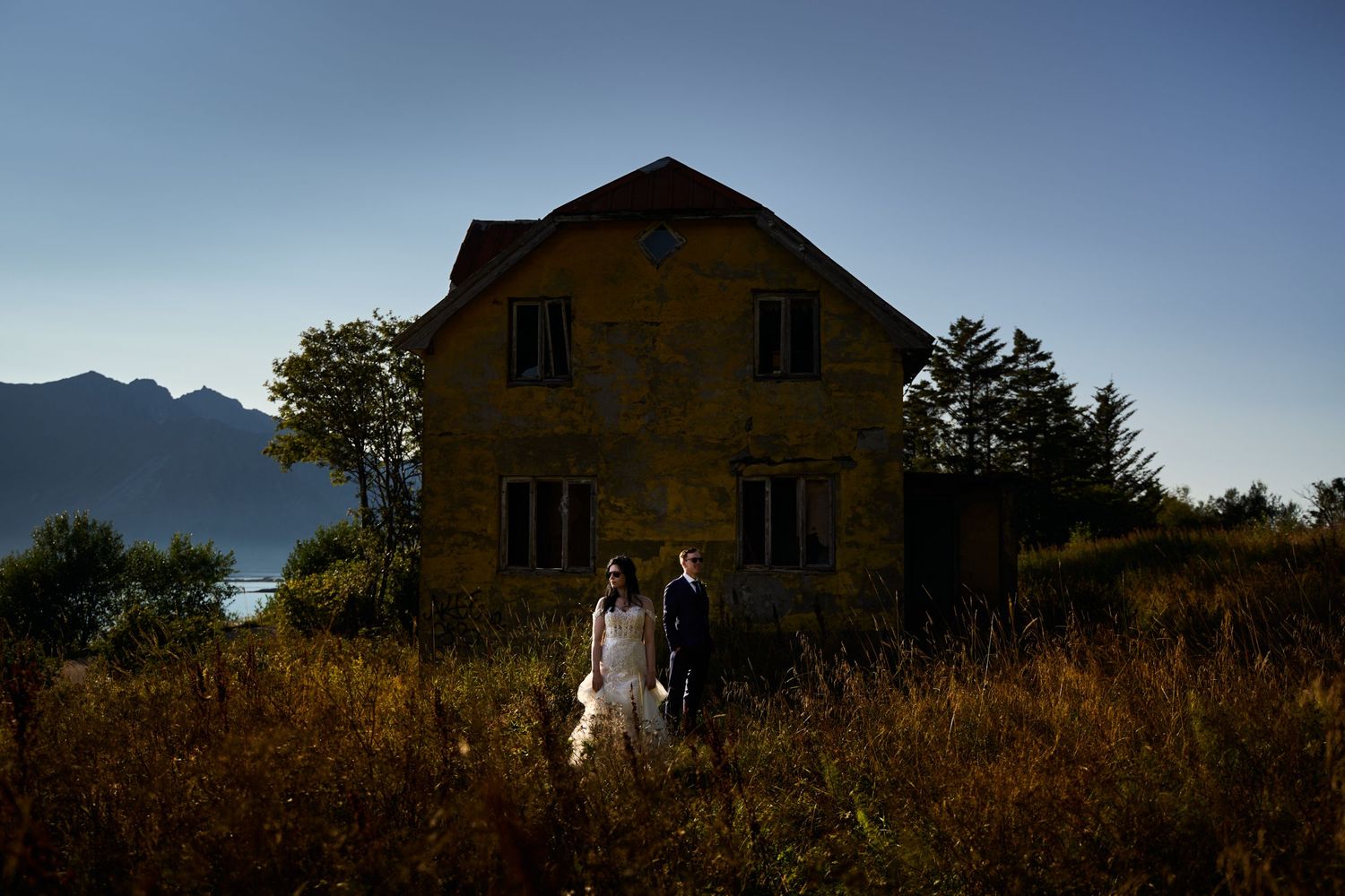 Bride and groom posing in front of a old, very rugged and worn house in golden midnight sun