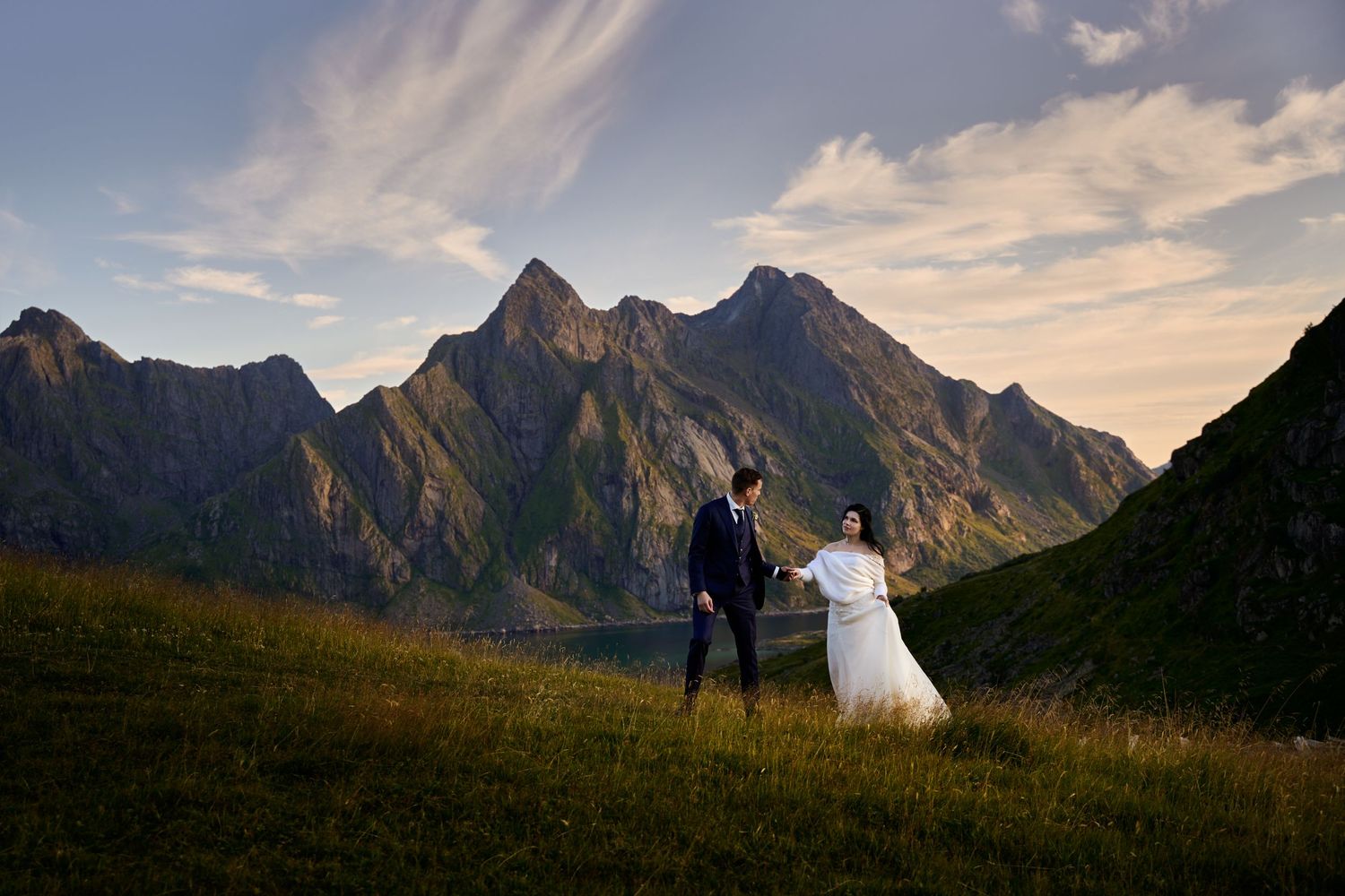 Bride and groom walking hand in hand in scenic surrounding with Lofoten mountains in the background at Undstad