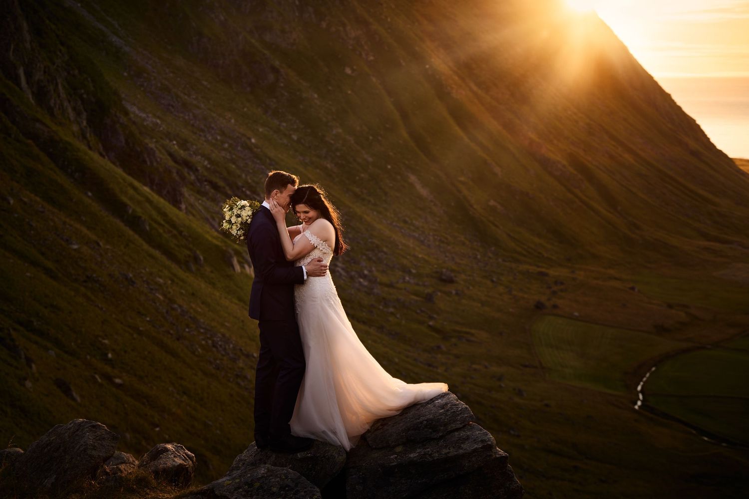 Bride and groom embracing each other amongst the Lofoten mountains in golden midnight sun