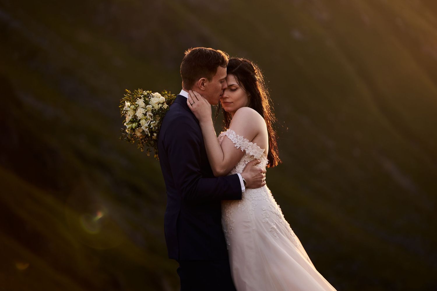 Bride and groom embracing each other amongst the Lofoten mountains in golden midnight sun