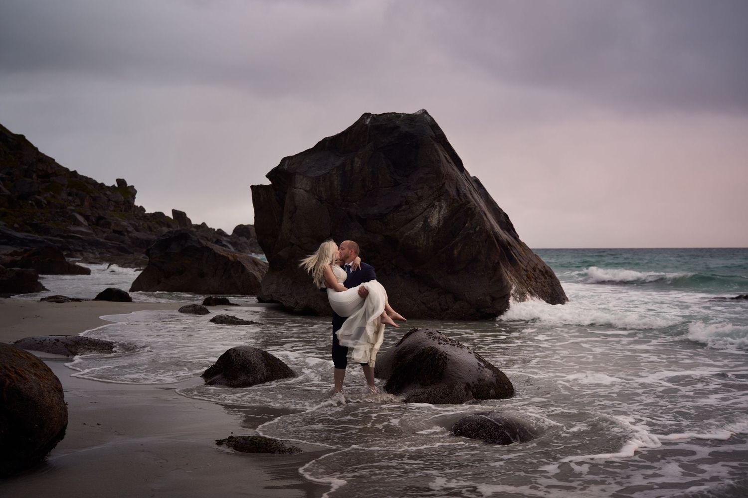 Groom carrying his bride on the Uttakleiv beach, Lofoten with pastel skies covering the midnight sun