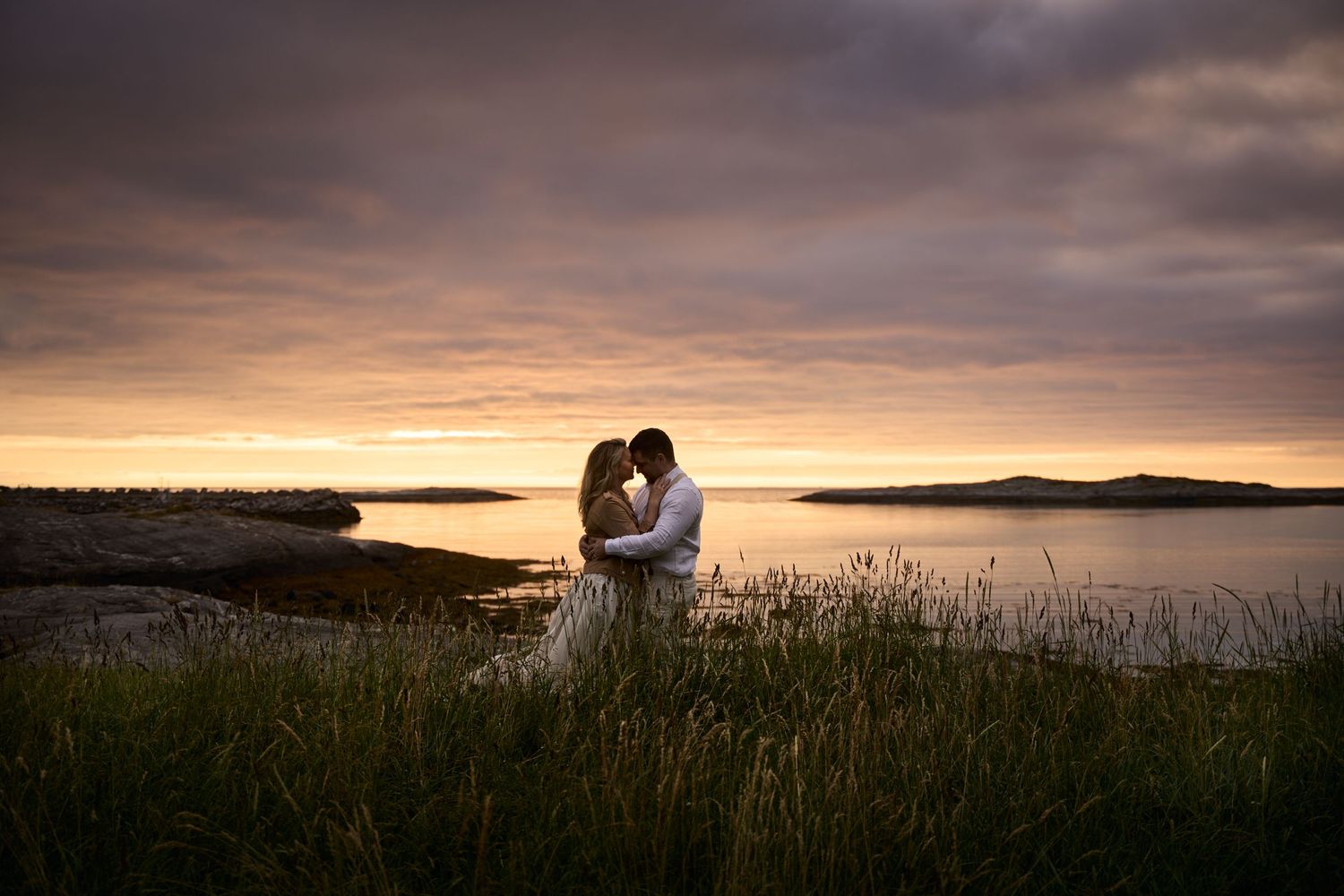 Bride and groom embracing each other on the beach in midnight sun