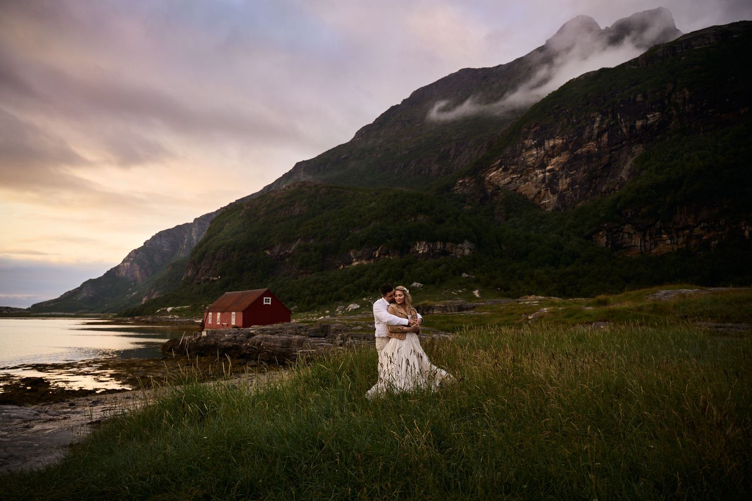 Bride and groom embracing each other amongst the mountains in pastel midnight sun