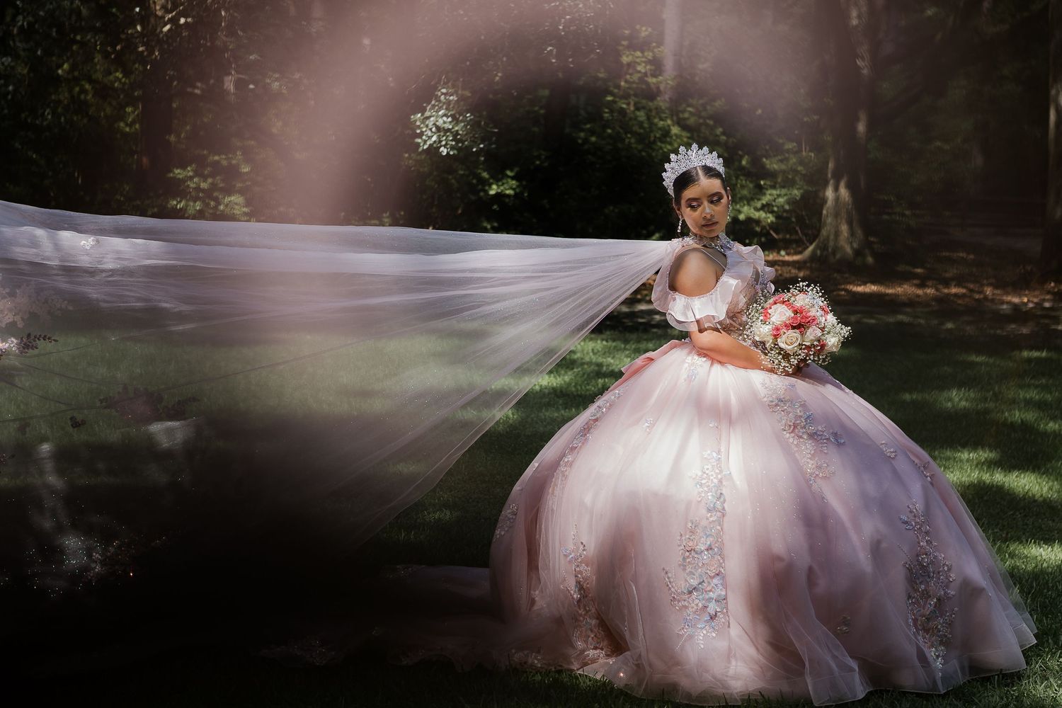 A person wearing a pink tulle ballgown poses gracefully in a garden setting with natural lighting and floral accents.