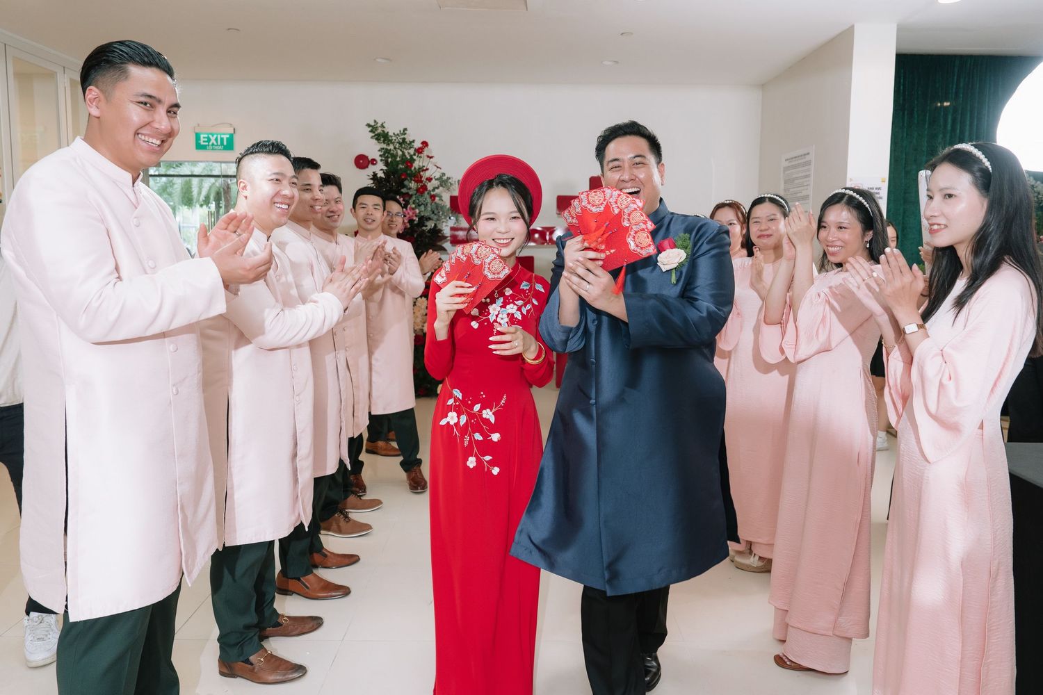 Vietnamese wedding couple in traditional red ao dai walking through an aisle of applauding guests in pink ao dai attire.