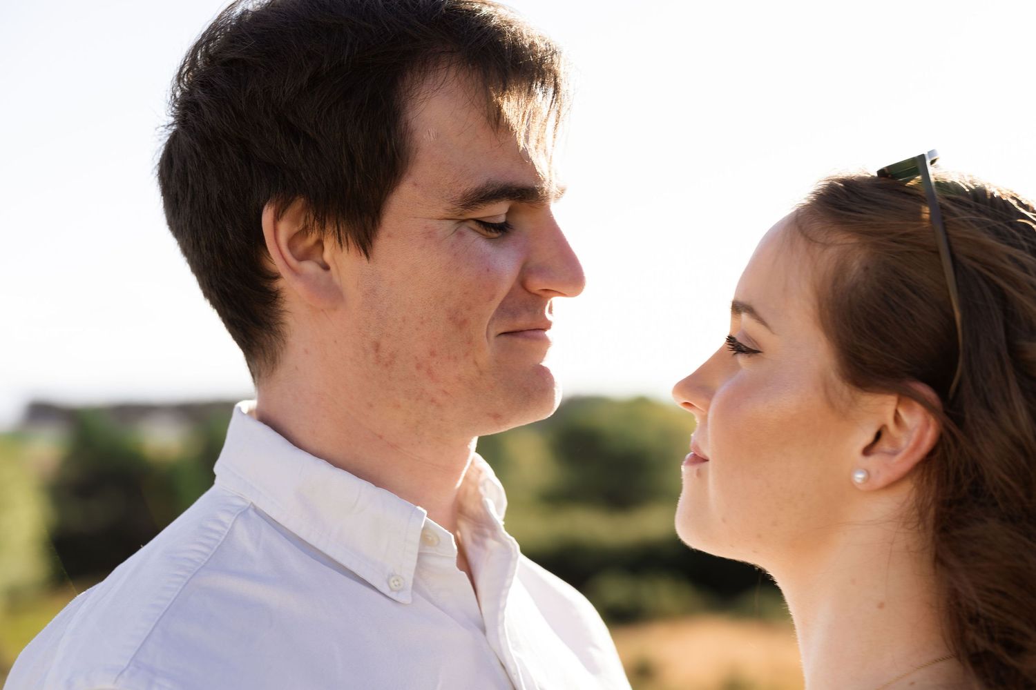 A tender romantic moment between a couple against a sunlit outdoor backdrop in a wedding setting.