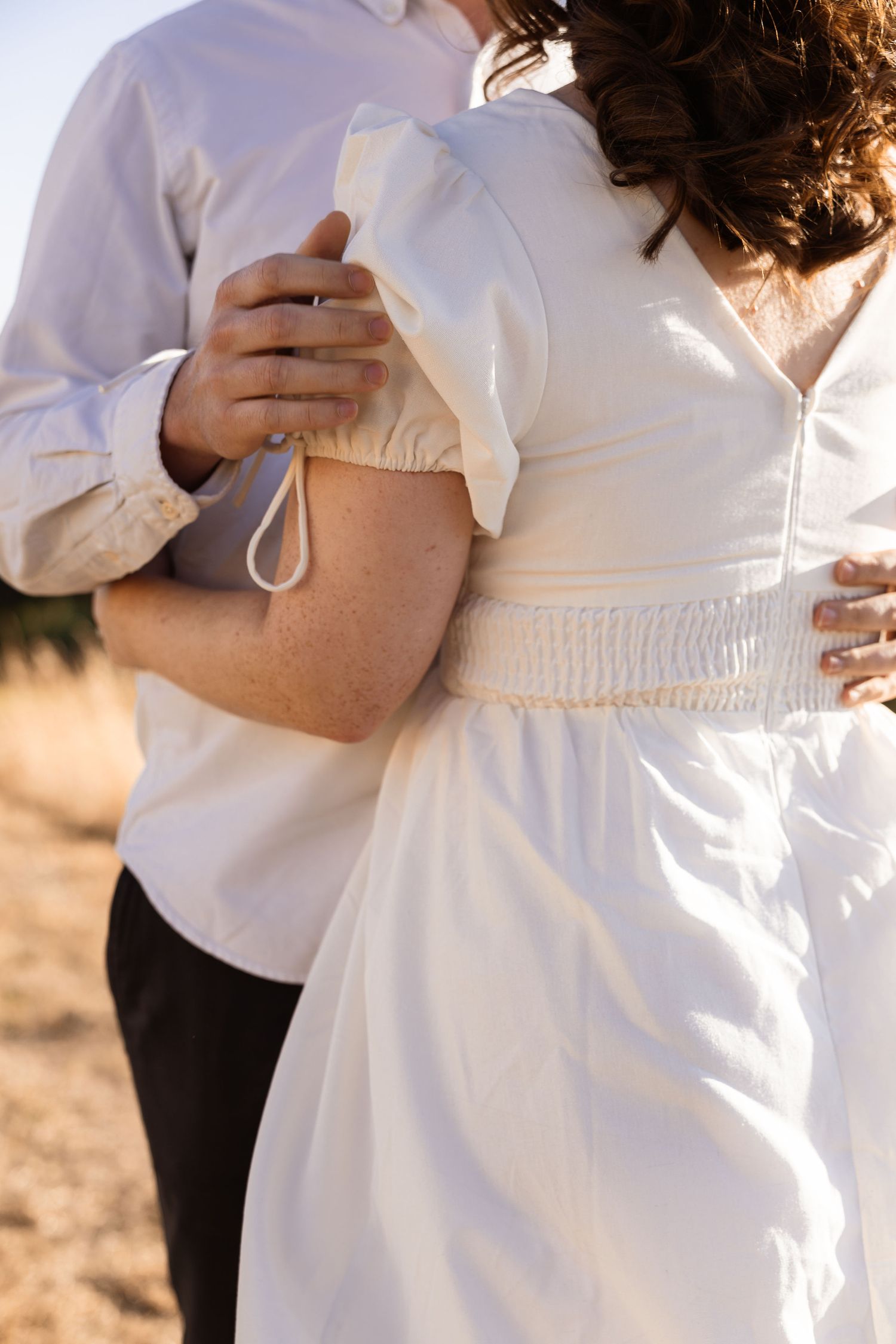 Close up photos of a white dress showing details like ties and belts at sunset with soft lighting outdoors.