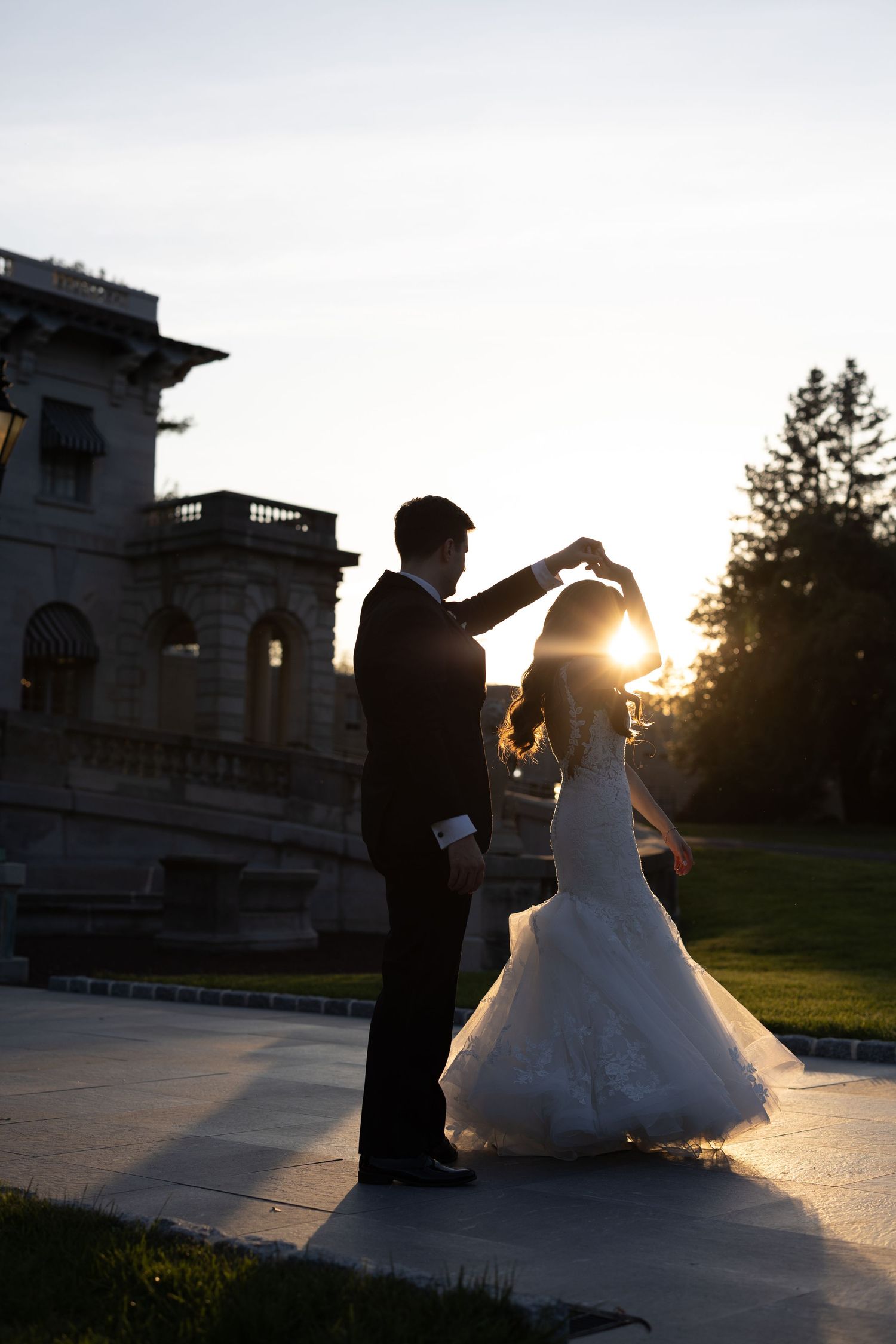 A romantic dance sequence between a couple in formal attire on a driveway outside an elegant mansion-style building.