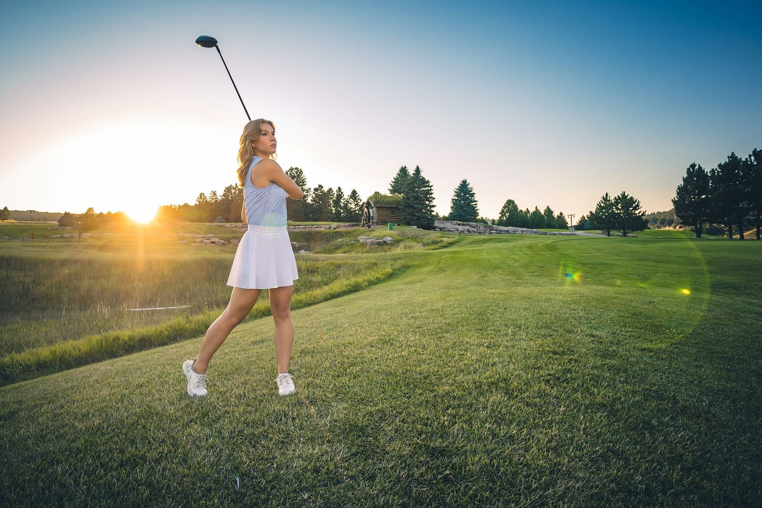 Golfer follows through with golf club on grassy course during golden sunset.