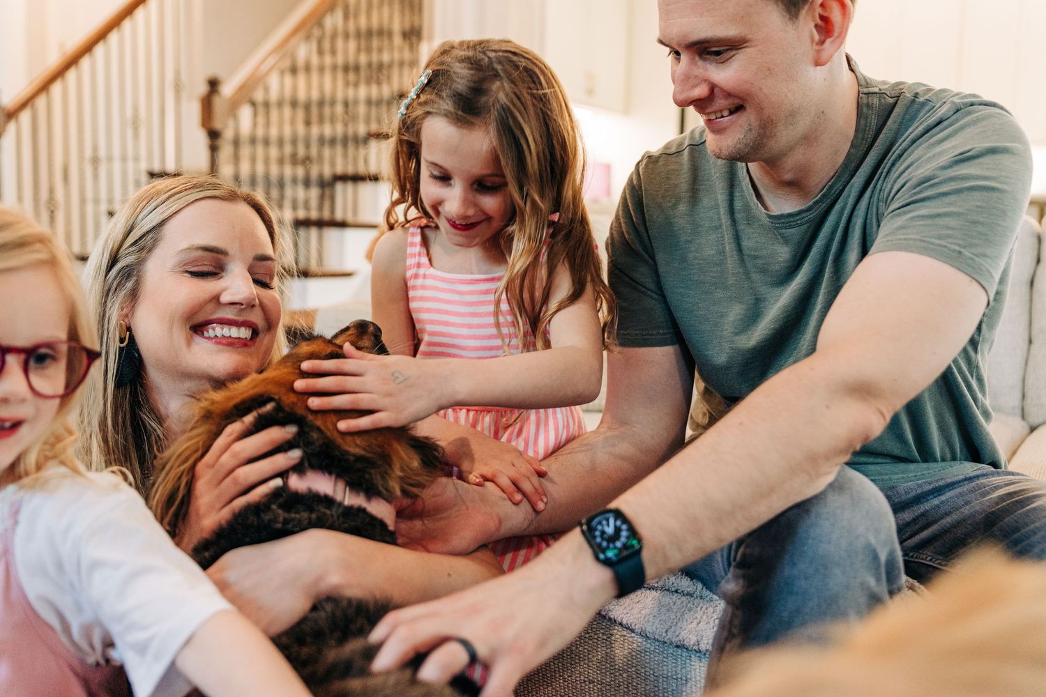 A happy family lounging together on a grey couch at home while sharing a lighthearted moment with their dog for Charlotte family photos
