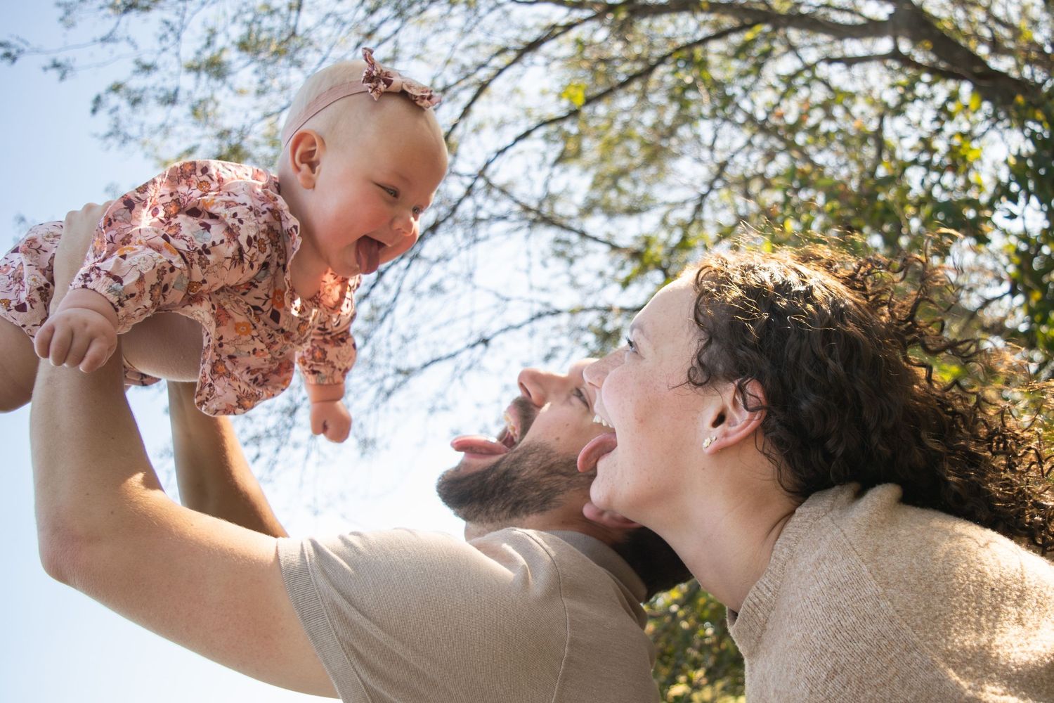 Couple holding their daughter above their heads, all sticking their tongue out at each other