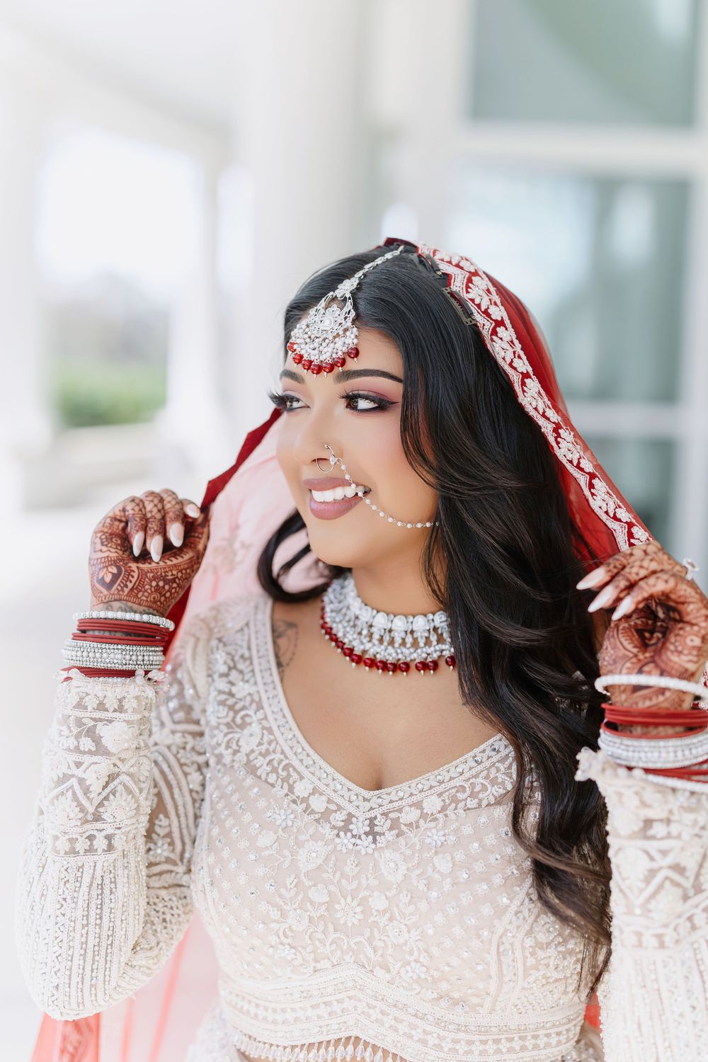 Close-up shot of South Asian bride in traditional white beaded dress and diamond jewelry laughing candidly.