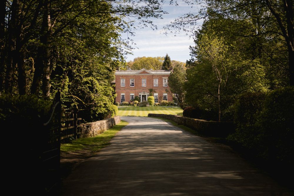 Tree-lined driveway leading to a stately brick building on a sunny day.
