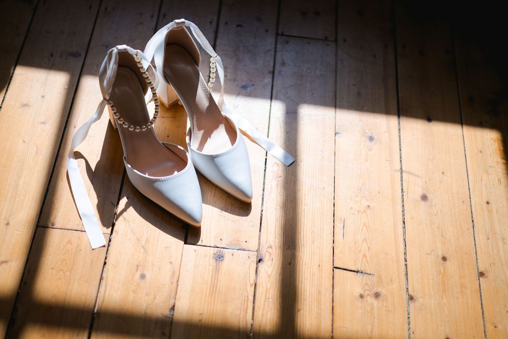 White wedding shoes arranged on rustic wooden floorboards with natural lighting.