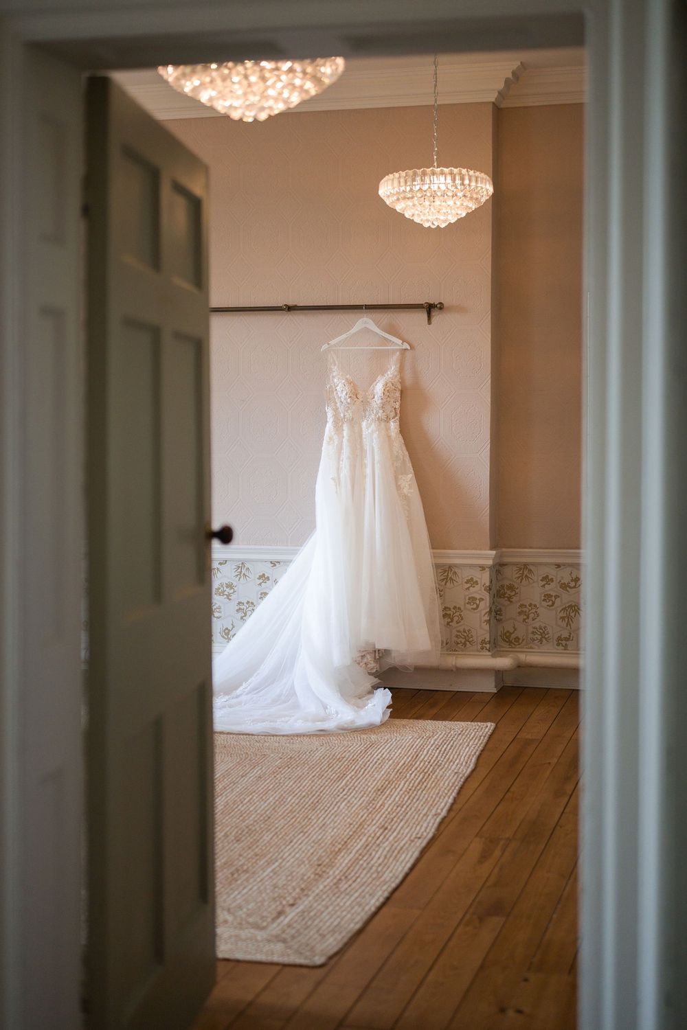 White wedding dress displayed on a hanger in an elegant room with crystal chandeliers.