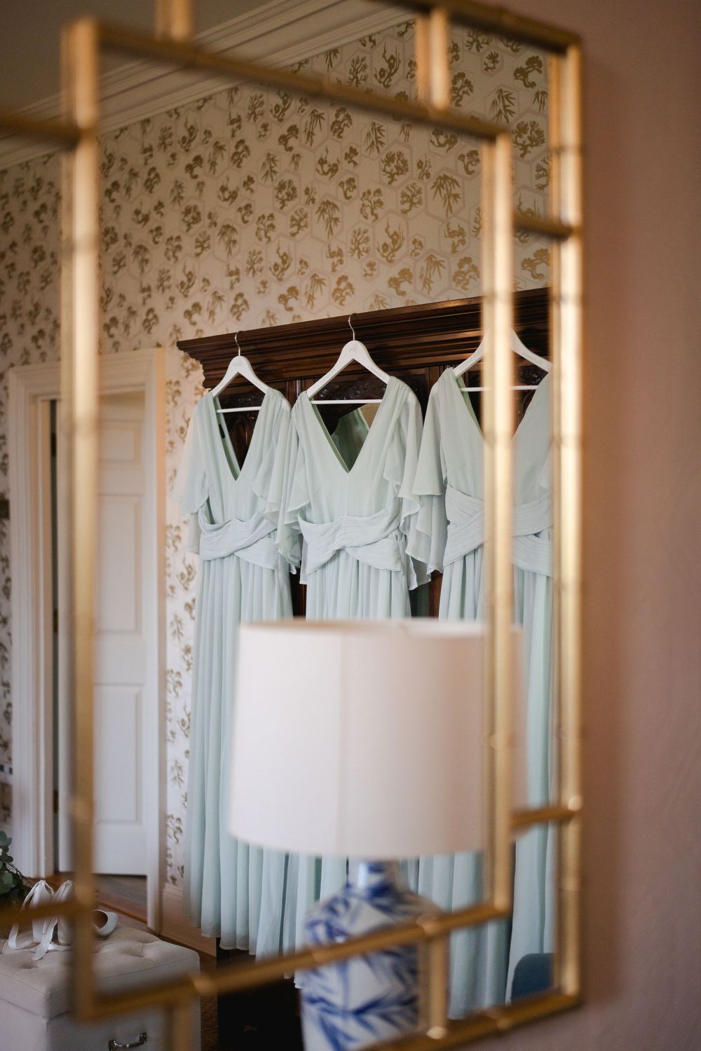 Pale mint bridesmaid dresses hanging on white hangers against floral wallpaper.