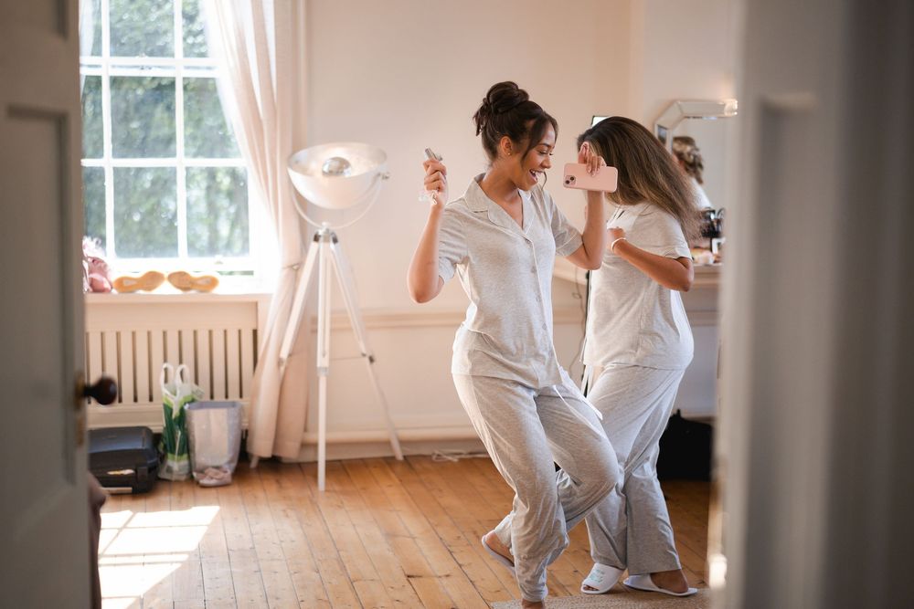 Two dancers in white outfits performing in a bright sunlit room.