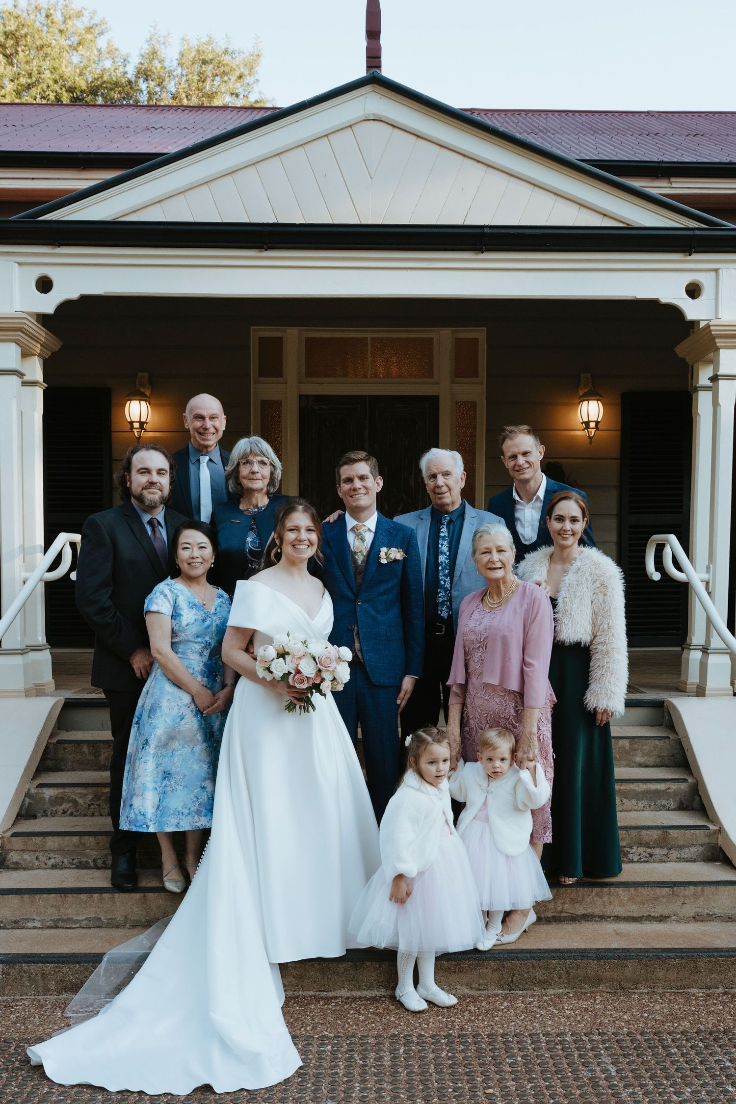 Wedding party members gather in front of venue entrance for formal group photos in mix of white dresses and dark suits.